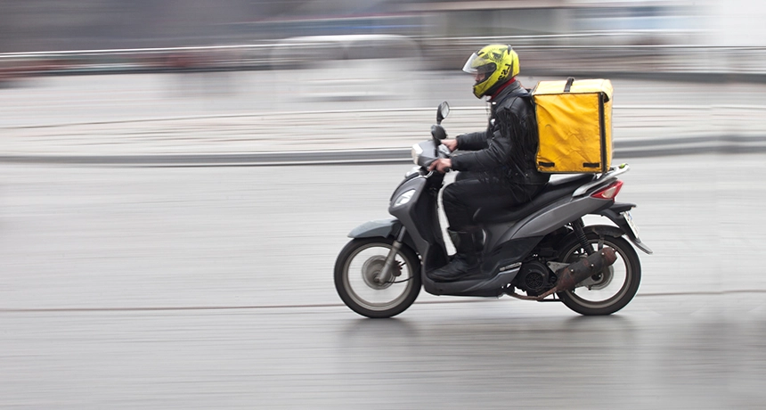 Person on a scooter on a road with a yellow top box