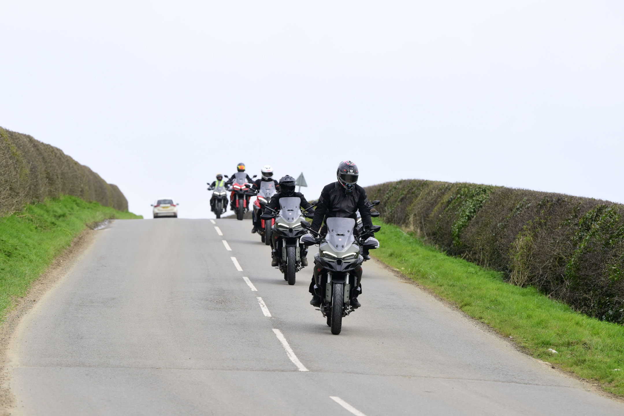 Multiple man riding Ducati touring bikes over a hilly road in the British countryside