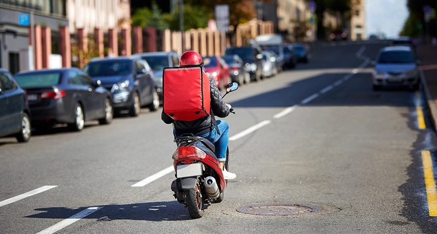 delivery rider on red motorcycle drives down road